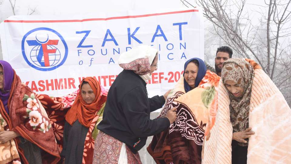 Woman bundled up in front of a Zakat Foundation sign.