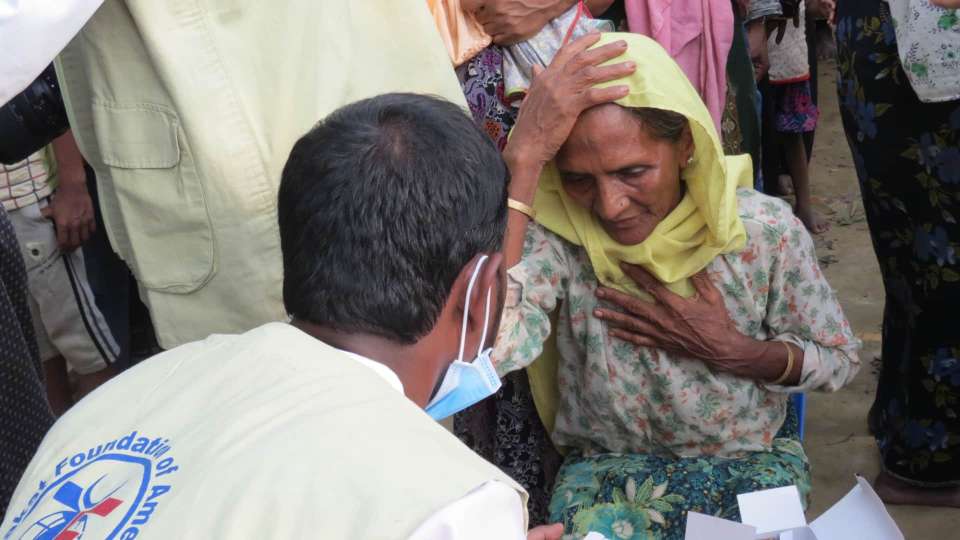 Old woman gripping her head talking with a Zakat Foundation member.