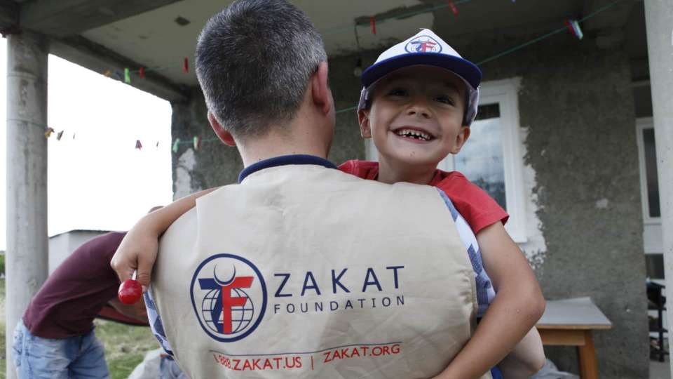 Zakat worker carrying a smiling child