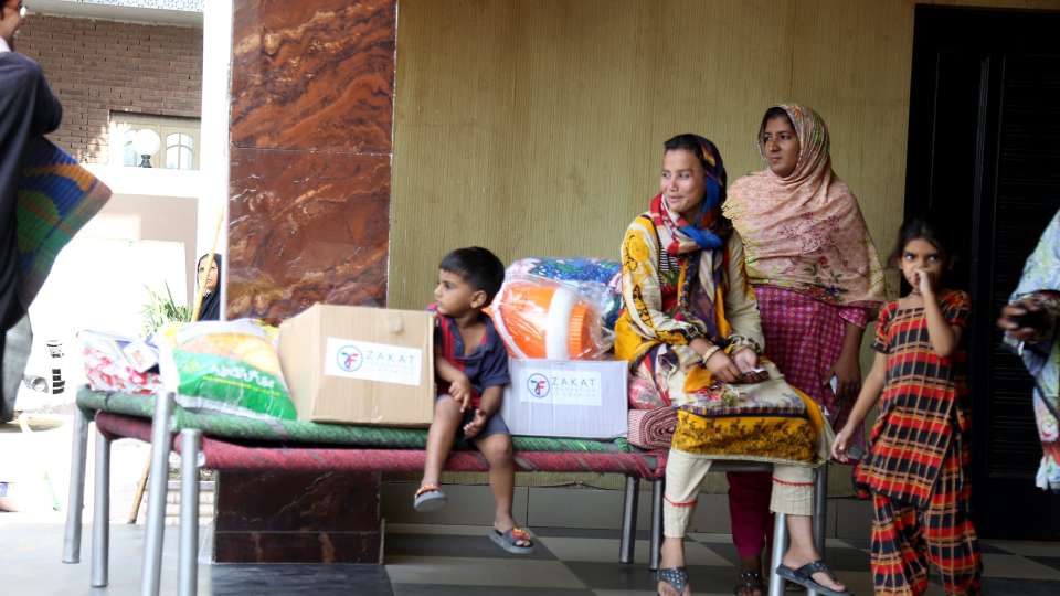 pakistani family of women and children smiling next to zakat foundation relief package