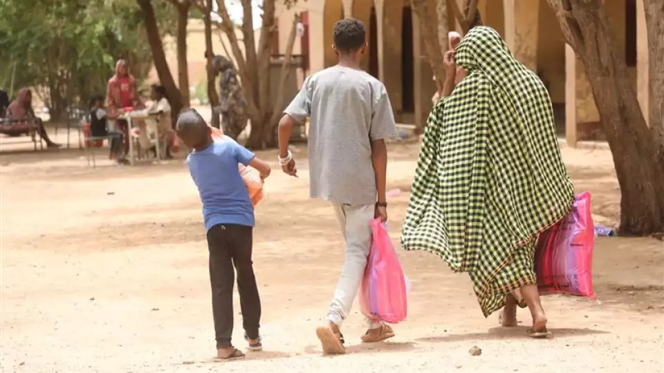 A Sudanese mother walks home with her children after receiving a food package that will give them nourishment