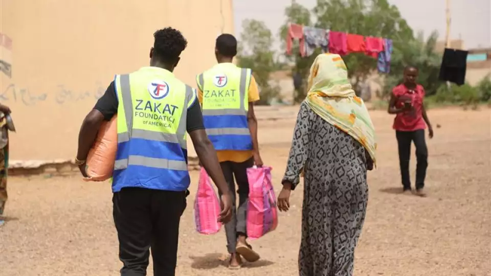 Our teams help carry supplies for an older woman displaced in Sudan