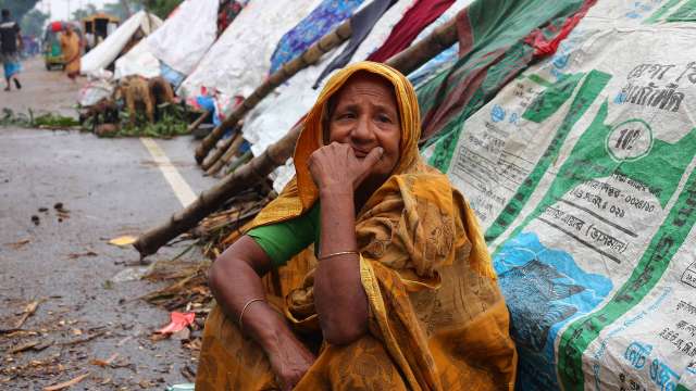 Elderly woman in Bangladesh sitting next to makeshift shelters due to flooding.