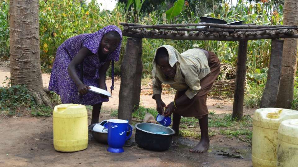 Zulea and Zaina washing dishes. Before they were sponsored by generous donors - they used to walk barefoot and would pull their clothes up to act as hijab.