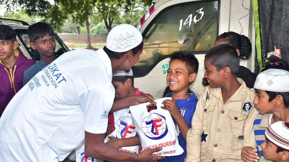 Zakat Foundation Volunteer handing Qurbani 2022 packages to smiling children in India.