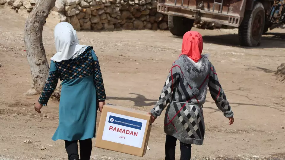 Girls in Syria walk home with a Ramadan food package
