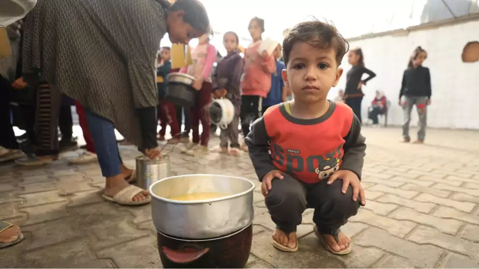 A young boy receives a warm meal from a community soup kitchen in Gaza