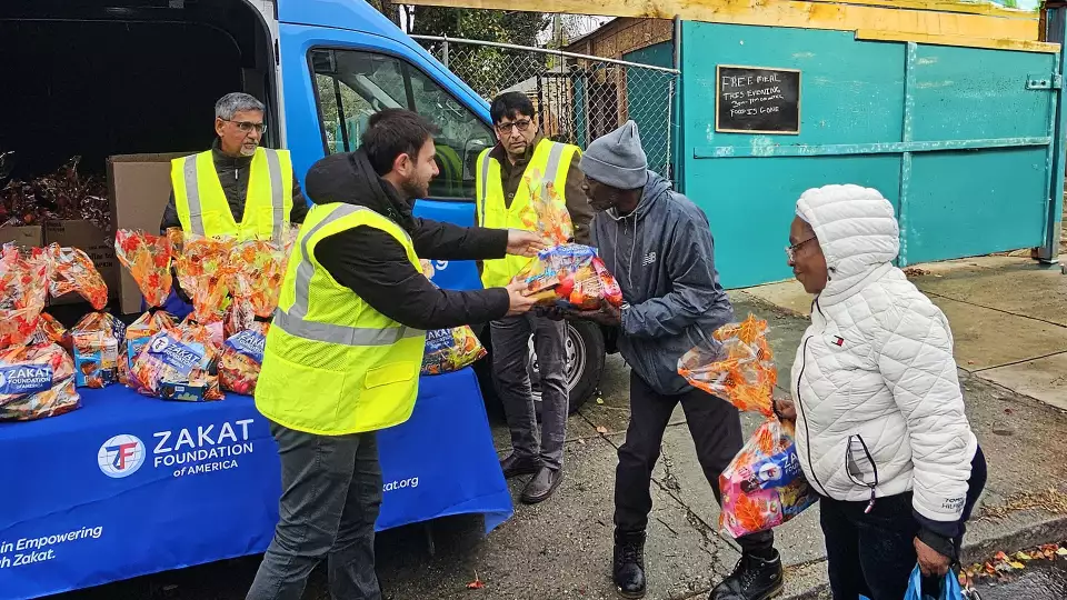 Image of Zakat Foundation of America relief worker handing food package to an African American couple.