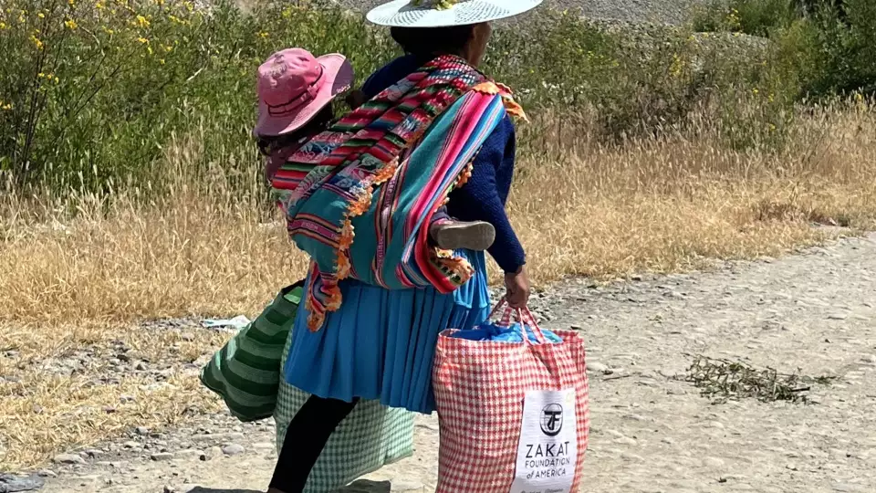 A Bolivian mother carries home our food packages and her child.