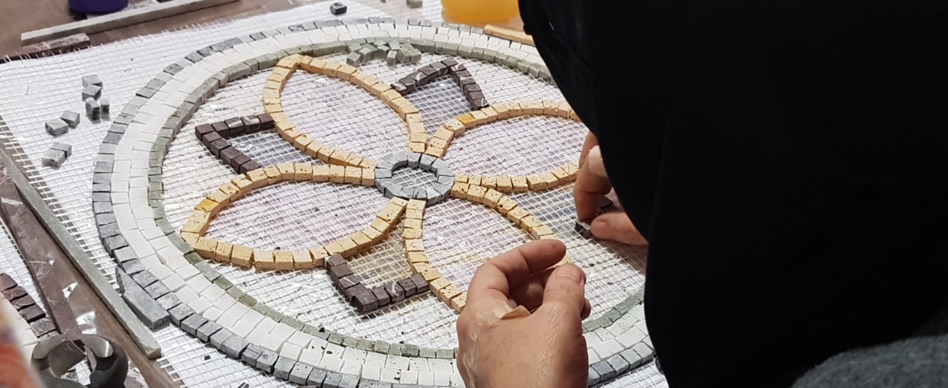 A person carefully arranges colorful tiles to create a vibrant flower mosaic, symbolizing creativity and resilience.